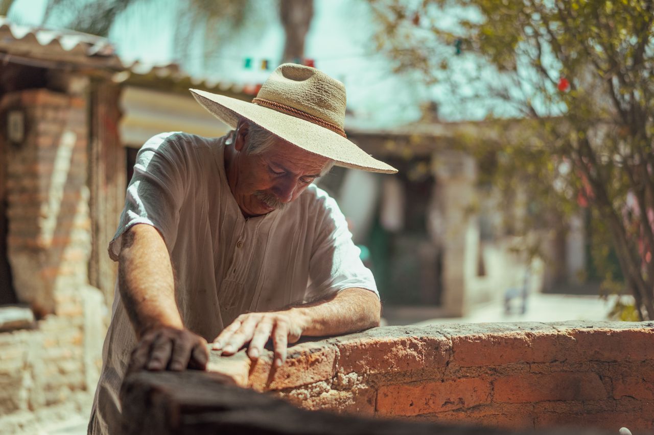 Senior man wearing sun hat working with bricks outdoors, showcasing craftsmanship.